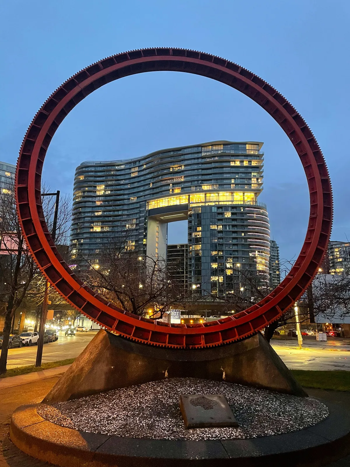 A huge gear-like decoration, through which you can see brightly lit buildings behind.